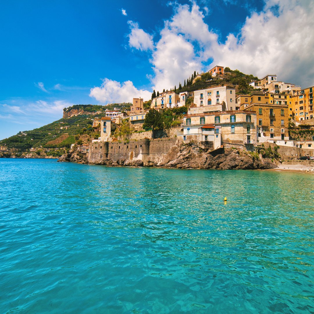 Un borgo pastello della Costiera Amalfitana visto dal mare, con le case impilate sopra l'acqua turchese e un promontorio scosceso