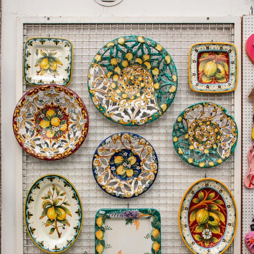 Una parete di piatti e vassoi in maiolica dipinti a mano con motivi di limoni e fiori, esposti in una bottega di ceramica a Vietri sul Mare